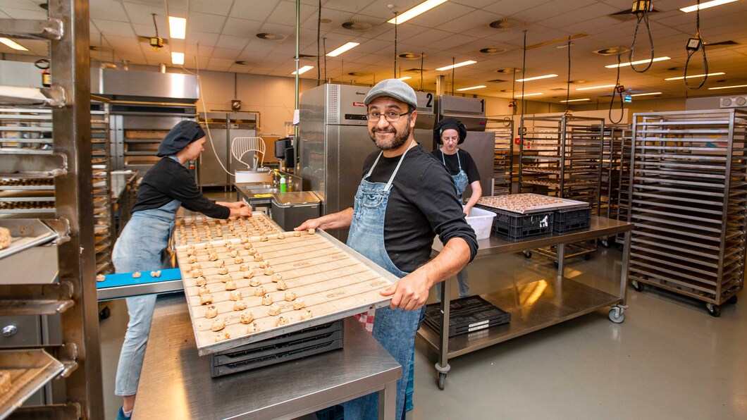 Man staat met bakplaat vol met koekjes in handen in een keuken en kijkt de camera aan.