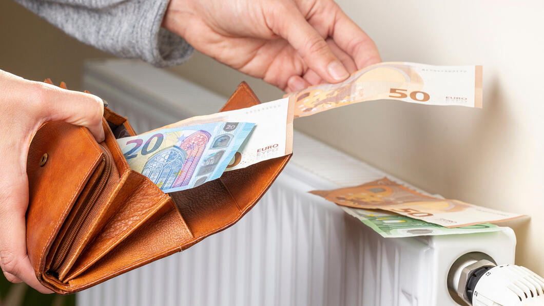 Woman's hand takes euro money banknotes from wallet and places on heating radiator battery with temperature regulator.